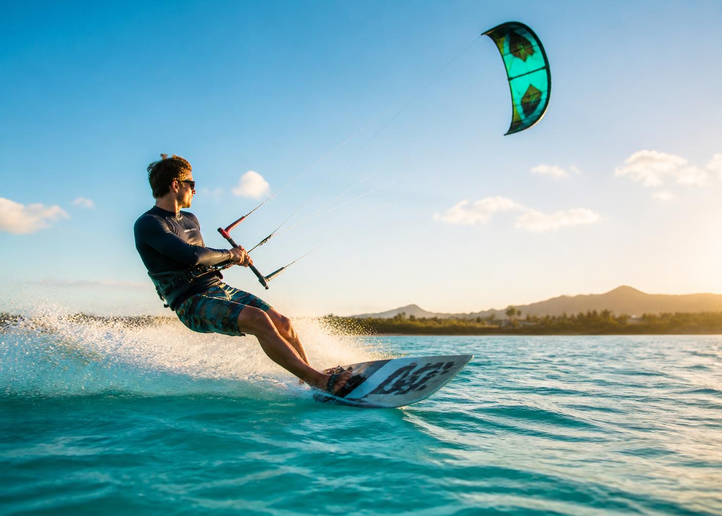 Kiteboarder gliding across turquoise water in late afternoon light